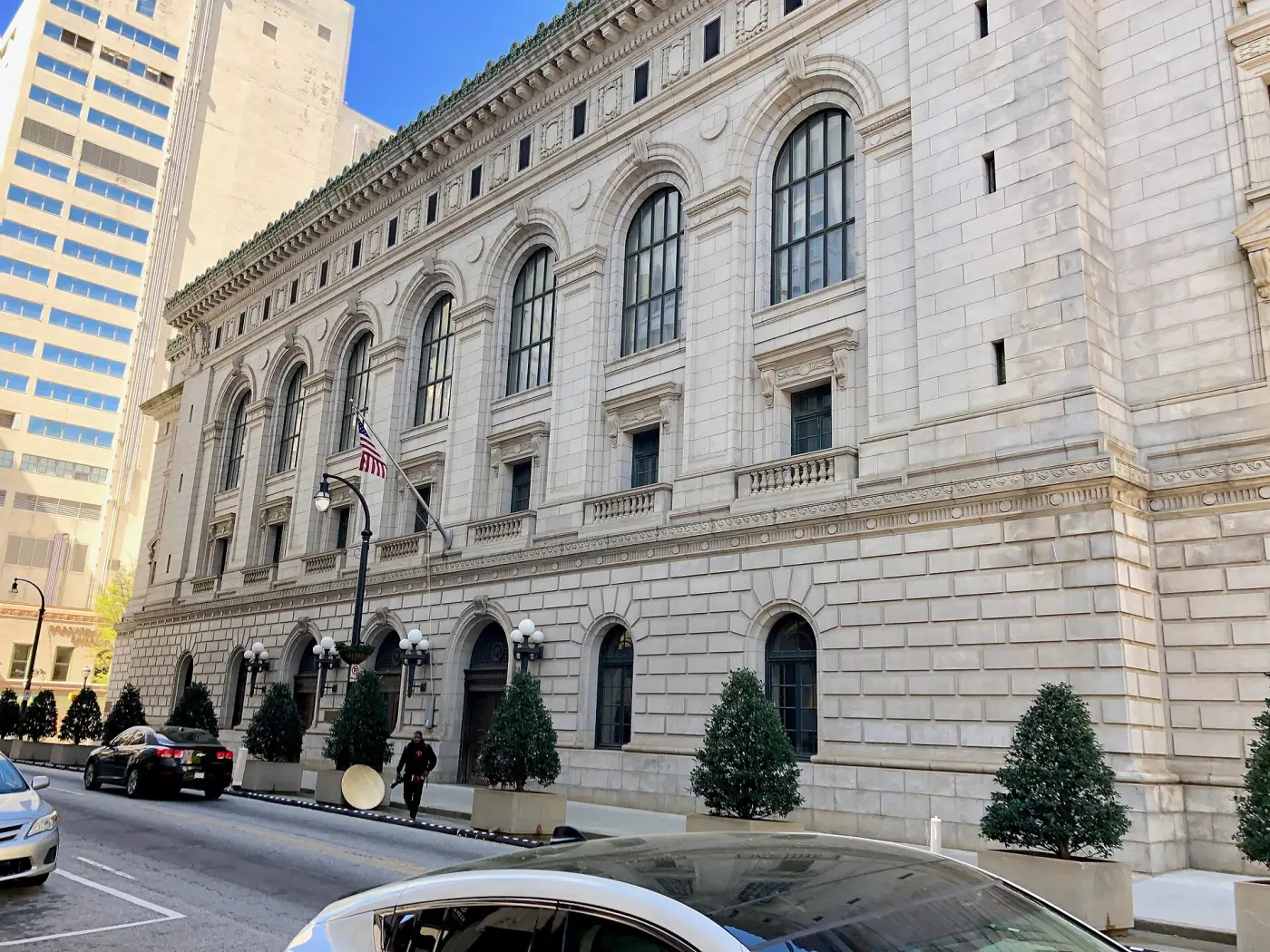 The stone facade of the Elbert P. Tuttle United States Court of Appeals Building in Atlanta, with arched windows, an American flag, and clipped trees along the pavement.