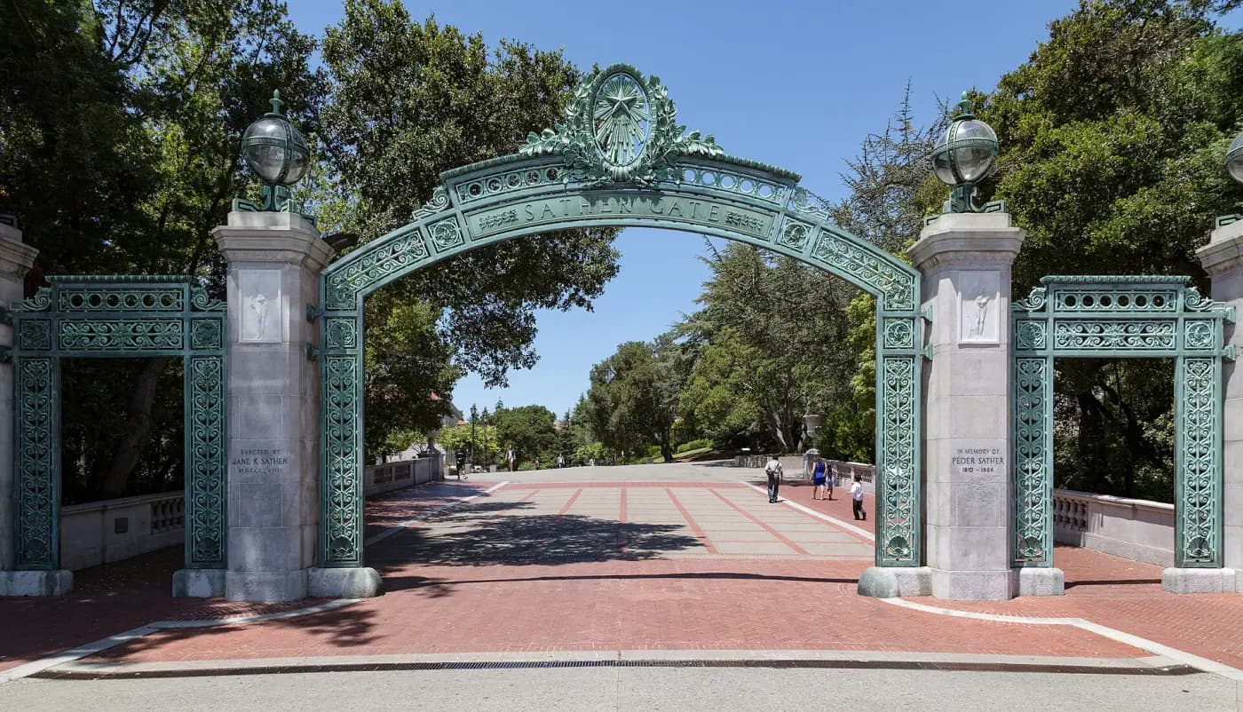 Sather Gate at the University of California, Berkeley: an ornate green bronze arch on stone pillars over a brick plaza, with a few students walking through.